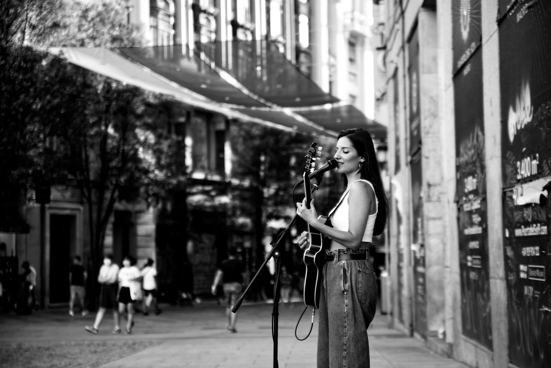 A female street performer plays guitar and sings in Madrid's lively streets.