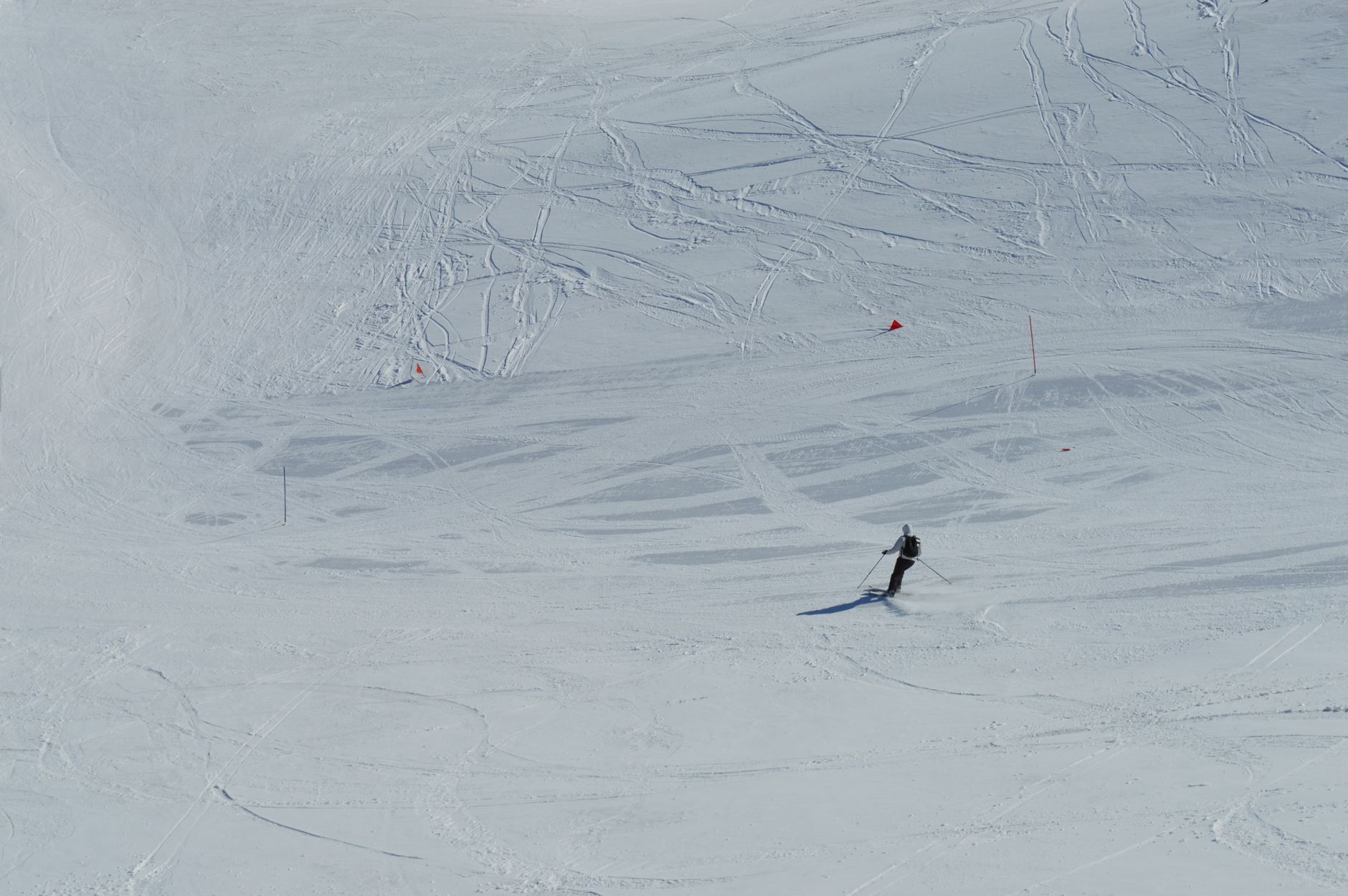 A lone skier traverses an expansive snowy landscape, leaving behind ski tracks on a sunny winter day.