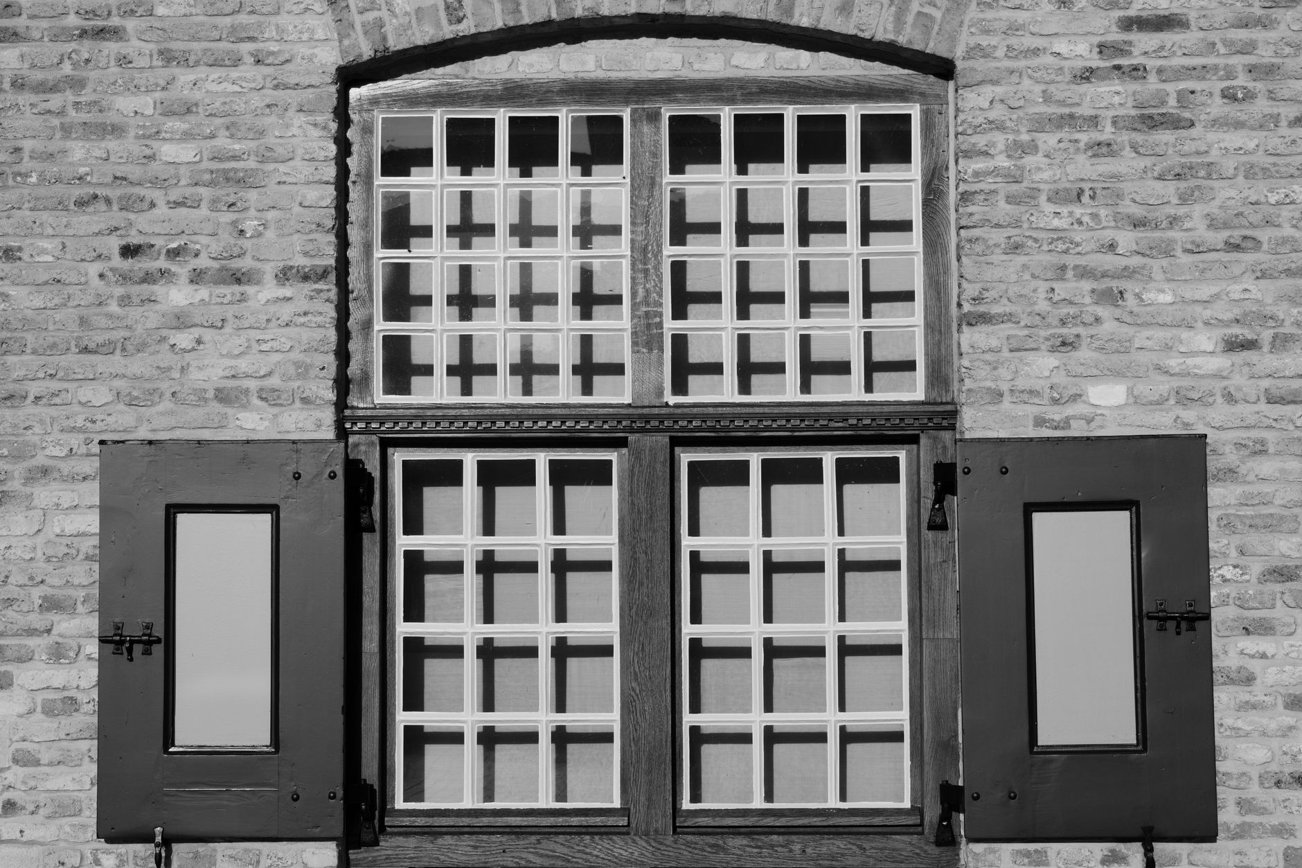 Black and white photo of a classic brick facade featuring wooden shutters and a grid window design.
