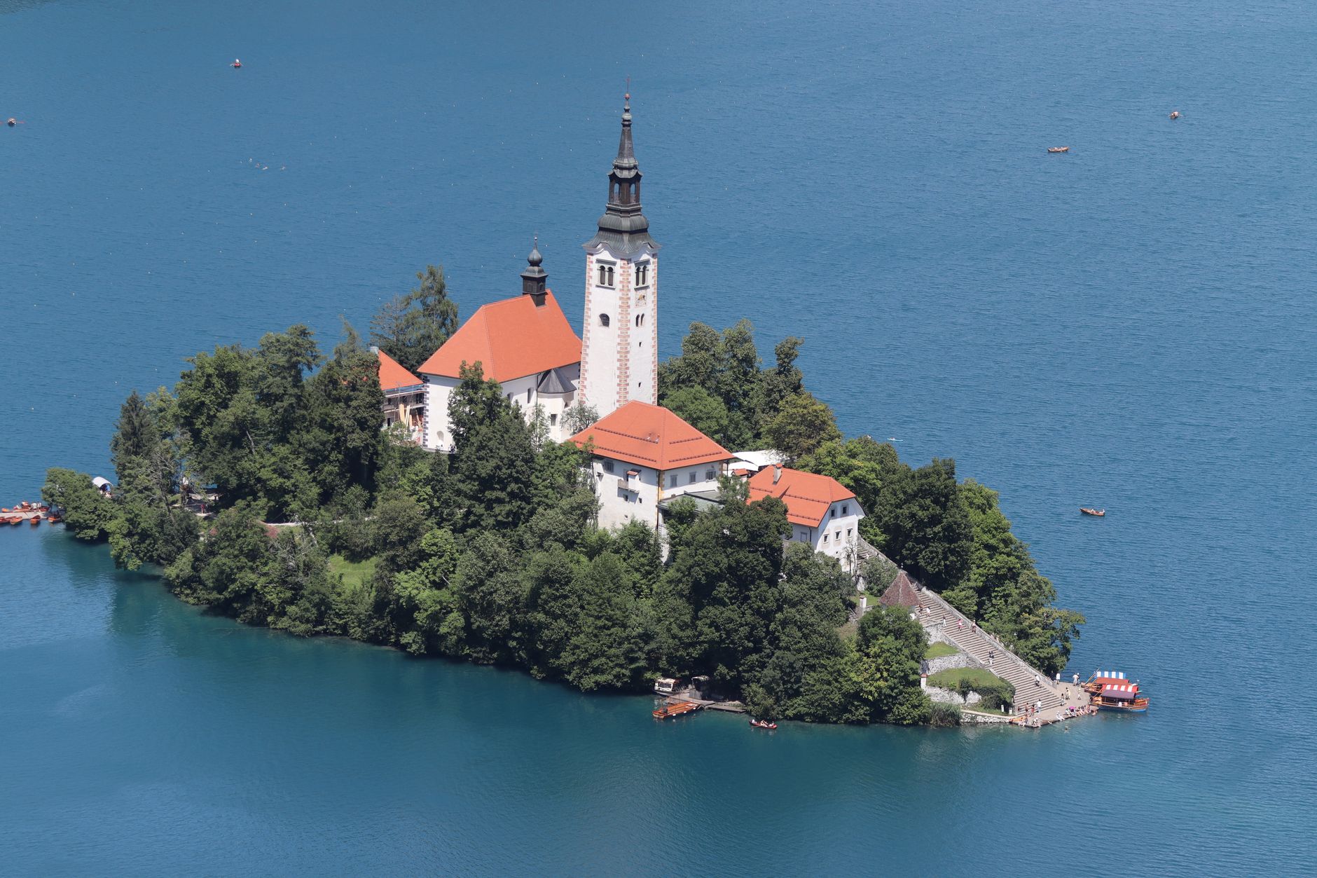 Stunning aerial view of Bled Island and church on Lake Bled, Slovenia, surrounded by crystal blue water and lush greenery.