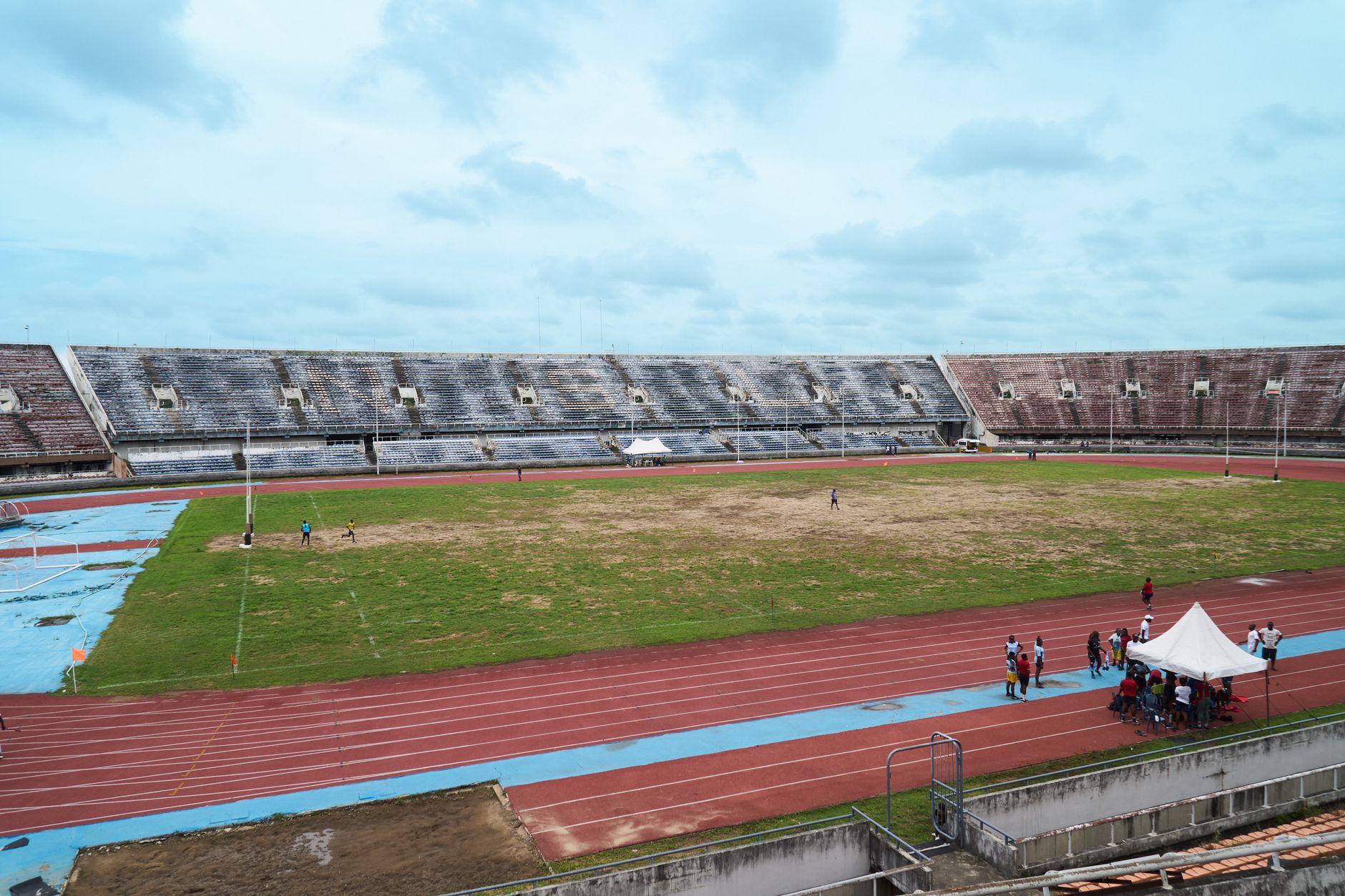 A spacious outdoor stadium with an empty field and surrounding running track under a cloudy sky.