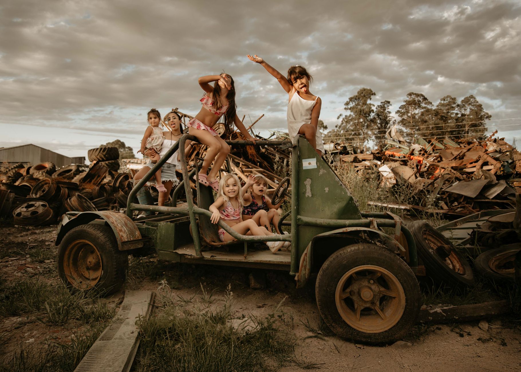 Group of joyful children playing on a makeshift vehicle amidst a rustic junkyard setting.