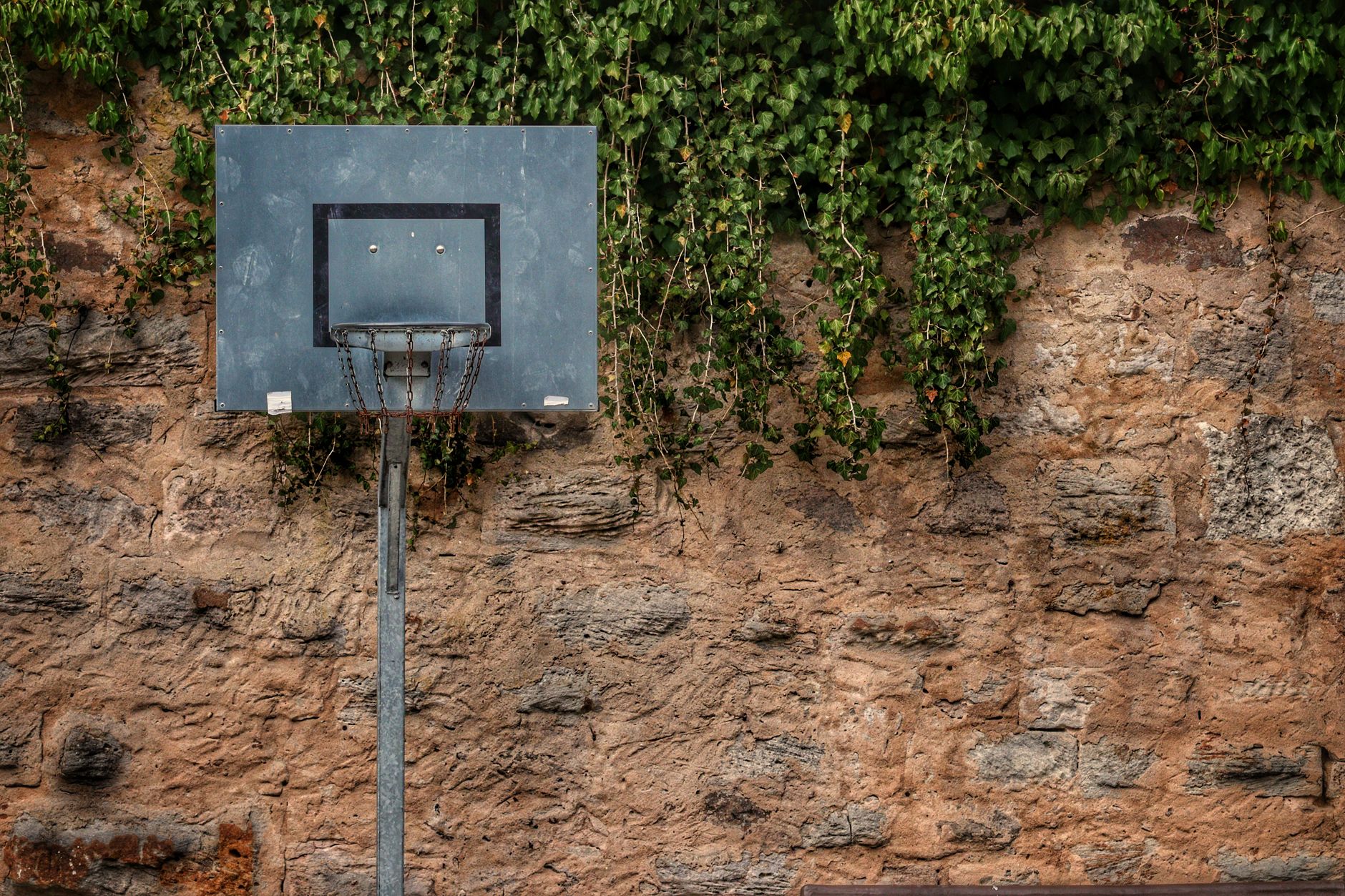 Lonely basketball hoop on old stone wall with greenery