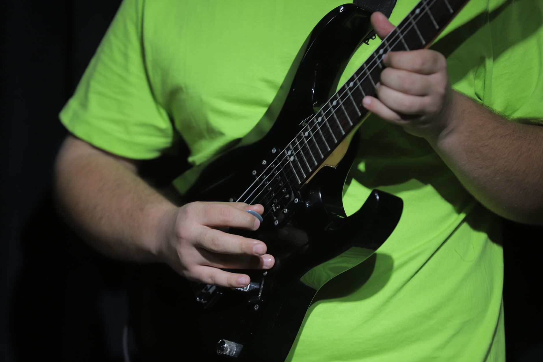 Musician playing electric guitar in a studio session, wearing bright clothing under stage lighting.
