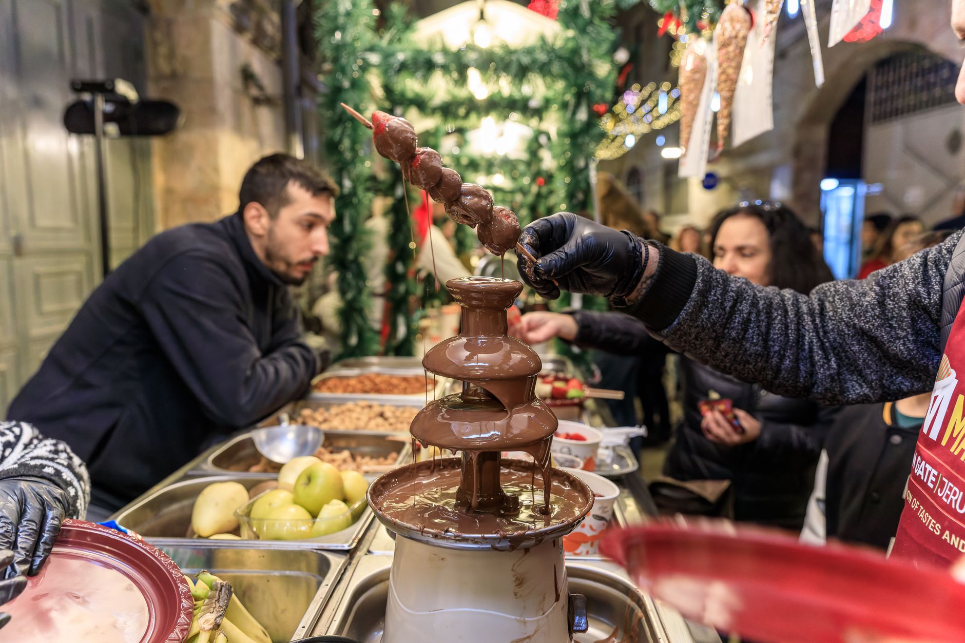 A vibrant scene of people enjoying a chocolate fountain at a festive outdoor market.