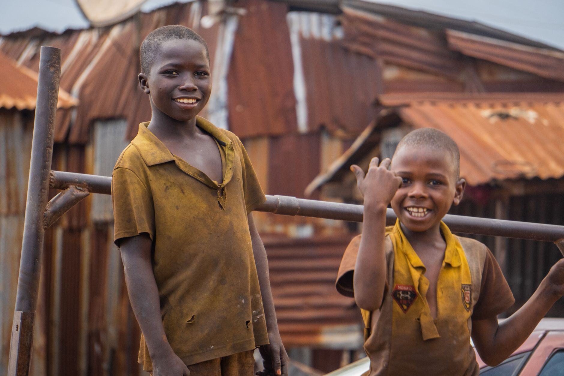 Two smiling children in rustic urban setting with corrugated metal background.